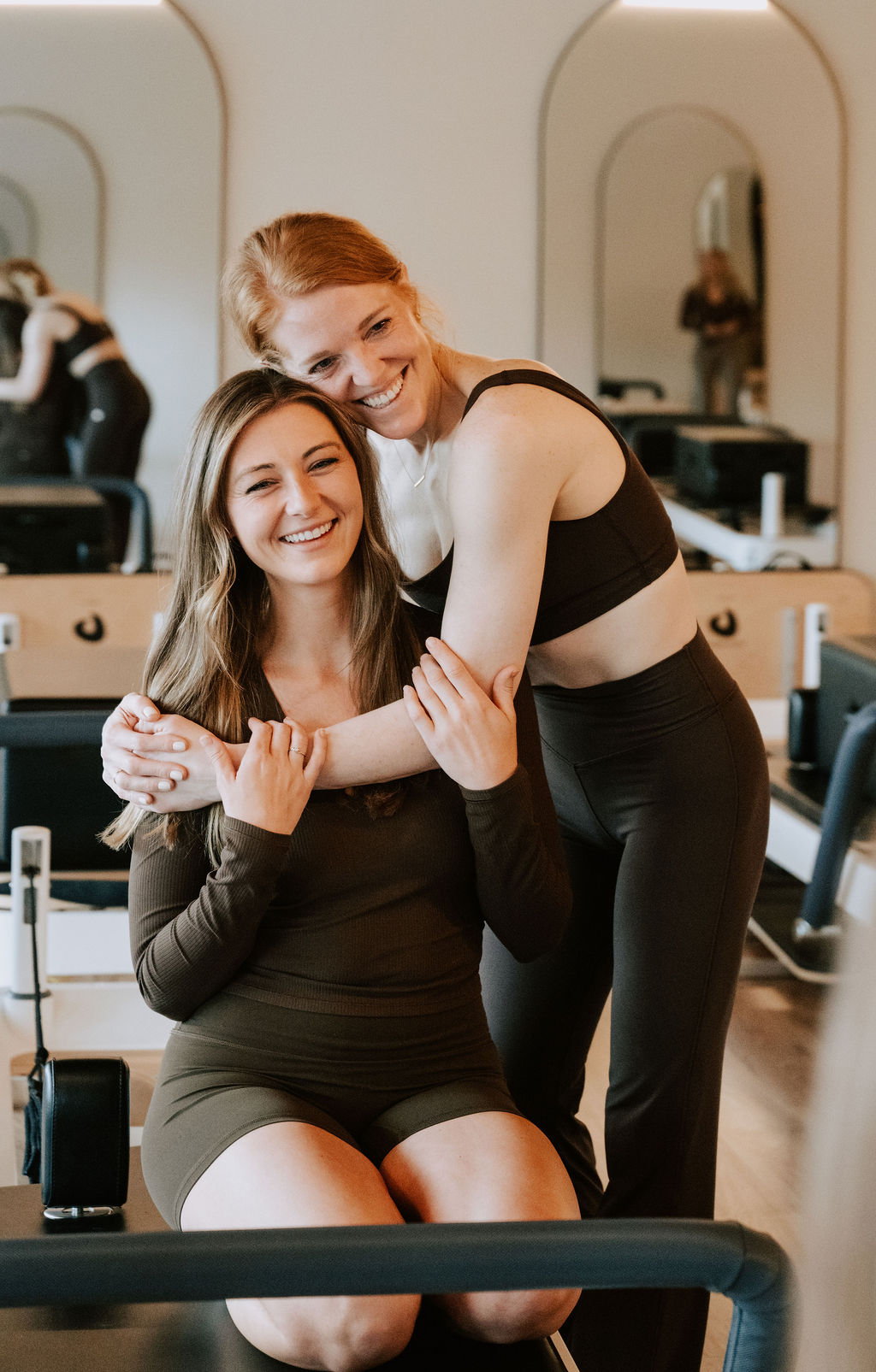 Two Core Collective members laughing together on a reformer